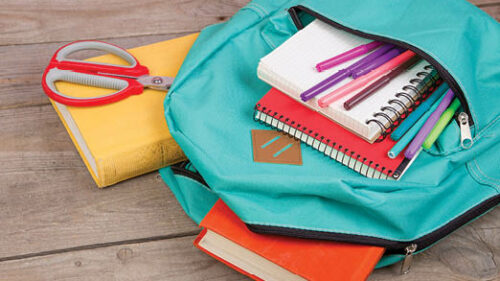 A book bag full of notebooks and pencils on the ground