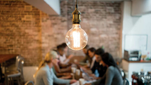 A group of people around a table with a very bright lightbulb in focus