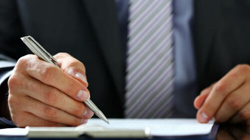 A business professional holding a pen and signing insurance paperwork.