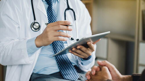 doctor holding an electronic device, discussing with a patient