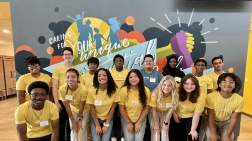A group of diverse high school students in front of a mural in the Waukee office