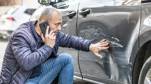A man examining a car that has been hit.