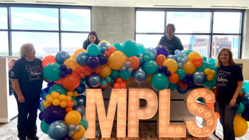 Four Holmes Murphy employees smiling around the letters MPLS with balloons celebrating their new office in Minneapolis