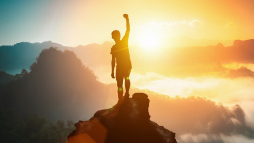 A person pumping their fist on the top of the mountain