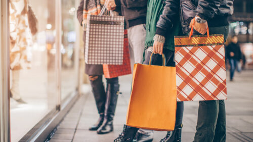 People looking at a shopping window carrying bags of previous purchases. It looks cold.