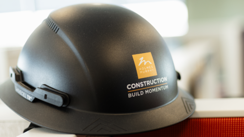 A black hardhat with an orange Holmes Murphy Construction logo